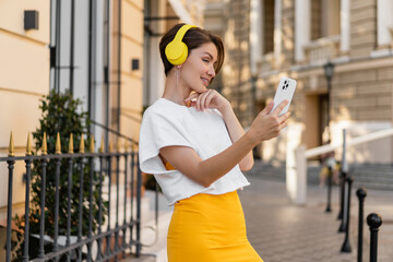 stylish woman wearing yellow headphones listening to music taking pictures on smartphone camera