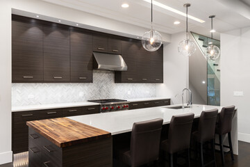 A kitchen with modern wood cabinets, a marble herringbone tile backsplash, lights hanging above the island, and white marble countertops. No brands or labels.