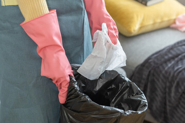 Tired household clean up, housekeeper asian young woman, girl hand holding tissue, napkin paper put in trash bin, cleaning in living room at home. Messy maid or housewife organizing dirty and untidy.