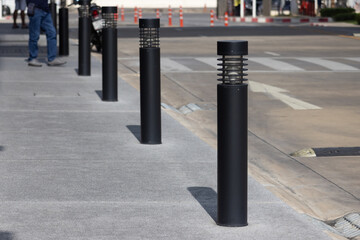 A row of black street lights are lined up on a sidewalk. light steel bollards on footpath.