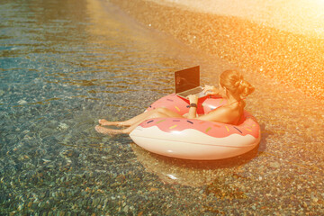 Woman laptop sea. Freelancer woman in sunglases floating on an inflatable big pink donut with a laptop in the sea. People summer vacation rest lifestyle concept