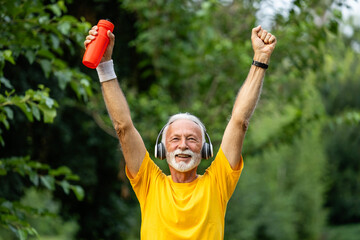 Senior man with arms raised crossing the finish line on marathon race.