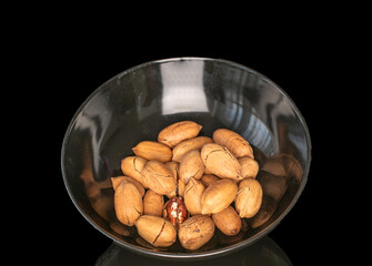 Several unpeeled pecans on a ceramic plate, macro, isolated on black background.