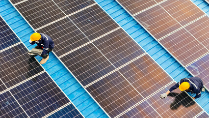 Photovoltaic engineers work on roof top warehouse. workers Inspect and repair the solar panel equipment roof structural. Engineer working set up electrical renewable energy for sustainability.
