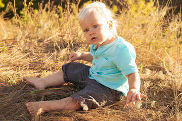 Baby boy with strabismus eyes on nature in summer sitting on grass with sun rays on sunset
