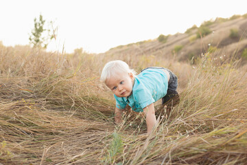 Baby child boy with strabismus eyes on nature in summer crawl on grass with sun rays on sunset