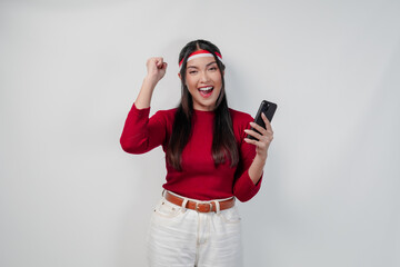 Excited Asian woman in a red shirt holding a cell phone and while raising fist.