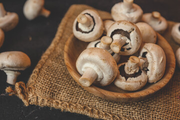 Champignon mushrooms in a wooden plate on a dark background