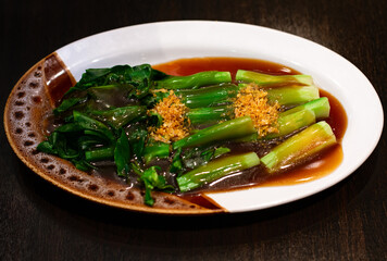 Hong Kong Kale stir fried in oyster sauce and dried garlic topping on white dish.Delicious Asian food.