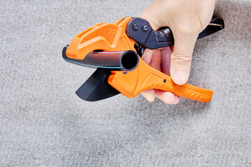Piece of plastic pipe lies between blades of pipe cutter with ratcheting mechanism, plumber hand...