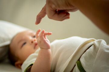 A baby is laying on a bed with a hand on its face. The baby is looking at the hand and the person who is touching it