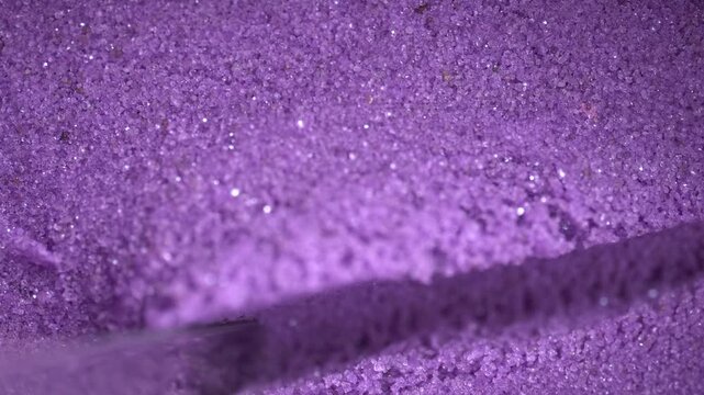 Metal spatula touching the purple kinetic sand. Textured, crumbly kinetic sand in lavender color. Kinetic sand background