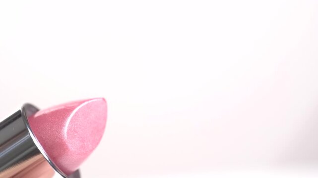 Close-up footage of pink shiny coloured lipstick rising out of its container against white background. 4K video. Make-up, cosmetics, beauty concept.