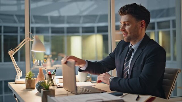 Smiling manager finish work on laptop at evening office closeup. Satisfied man