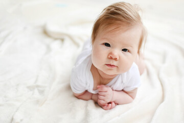 Portrait of a cute Caucasian 3-month-old baby girl during tummy time looking at the camera with the white background. Copy space.