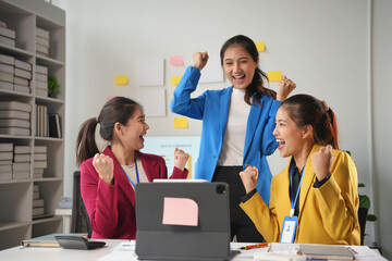 Three young businesswomen are raising their fists in the air, excited about achieving a business target