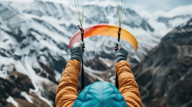 Image of a person paragliding in winter clothing, holding the canopy against a backdrop of snow-capped mountains, showcasing adventure and exhilaration.