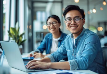 smiling man and woman in casual attire are sitting at an office desk with laptops, working together on digital marketing projects