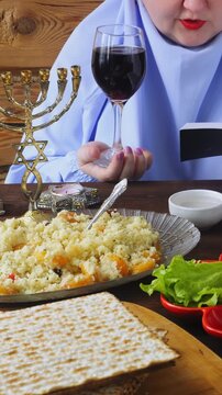 A Jewish woman in a blue veil at the Pesach Seder table reads kiddush with a glass of wine. Vertical video