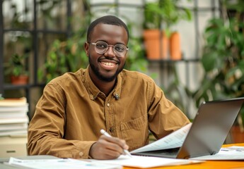 Happy young businessman working on his laptop at his desk in a modern office