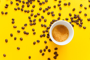 Cup of espresso and whole coffee beans on a yellow background