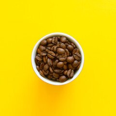 Small espresso cup with whole coffee beans on a yellow background