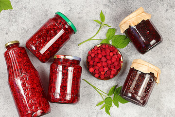 Jars with raspberry jam and compote on a light background with leaves and berries, home canning...