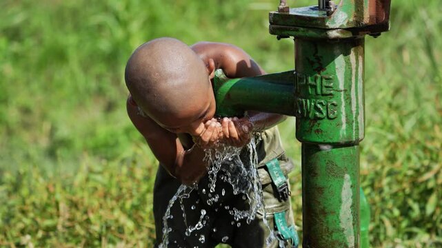 A child drinking and washing his head from a handpump tube well, highlighting the importance of saving water and addressing drinking water scarcity in rural areas.