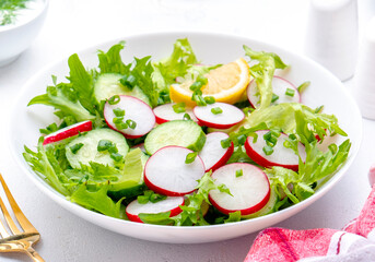 Summer vegan crispy salad with cucumbers, radishes and lettuce, white background, top view