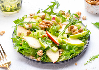 Delicious crispy vegan salad with green and red apples, fresh celery, lettuce, arugula and walnuts on plate, white background, top view