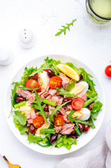 Tasty salad with tuna, tomatoes, eggs, beans, lettuce and olives with mustard dressing on white background, top view