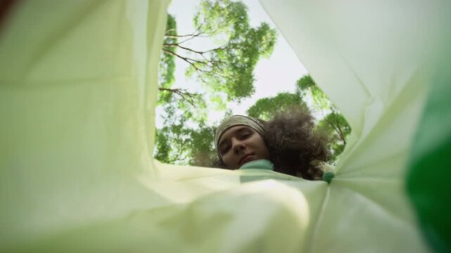 Below view from inside of rubbish sack of faces of young diverse eco activists throwing plastic litter gathered during forest cleanup into bag for proper disposal and recycling