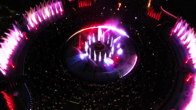 Aerial footage of the light show of the Bucharest fountains on a summer evening. Drone shot of the magnificent lights illuminating the mesmerizing dancing water fountain. Tourist attraction in summer.