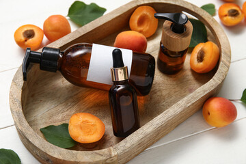 Tray with bottles of different cosmetic products with fresh apricots on white wooden background