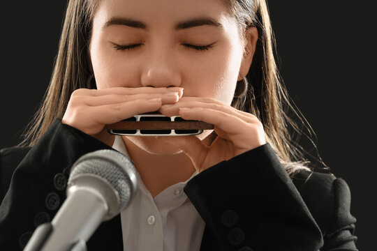 Female artist playing harmonica on dark background, closeup