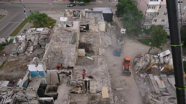 Timelapse shows crane dismantle war-damaged building in urban area. Workers clear rubble, remove concrete slabs from residential site. Demolition process accelerates in fast motion. Timelapse