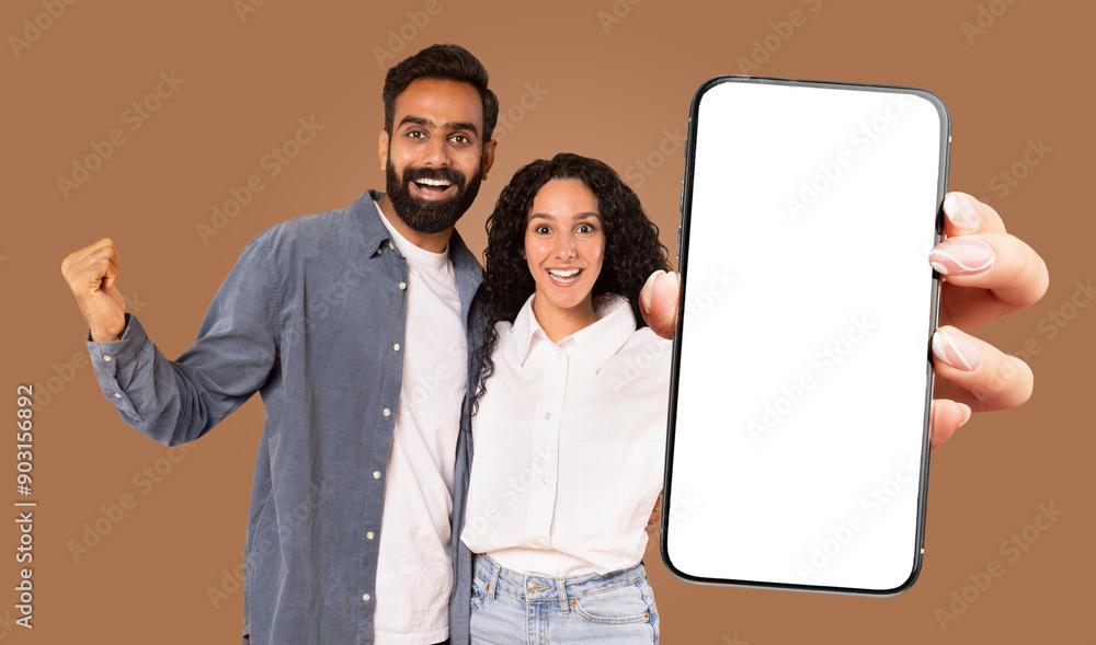 Poster a happy multiracial couple is standing in front of a brown background, holding a large smartphone wi