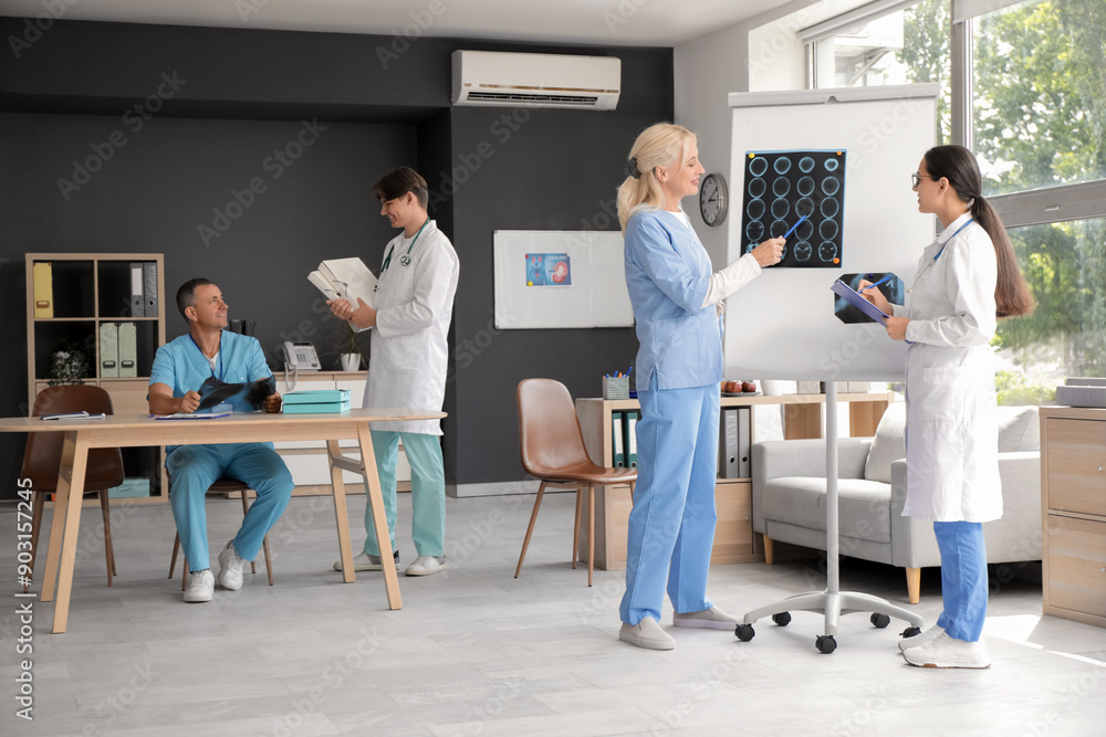 Poster Female doctors studying x-ray images on flipchart in clinic