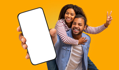 A smiling young black couple is posing against a bright yellow background. The man is wearing a...