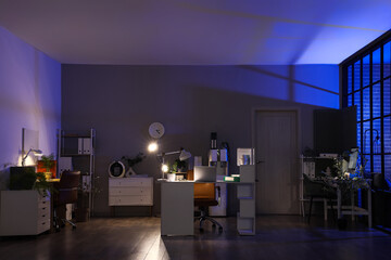 Interior of dark office with desks, shelf units and glowing lamps