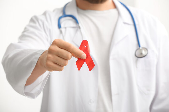 Doctor with stethoscope and red ribbon on white background, closeup. Blood Cancer Awareness Month