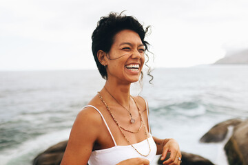 Carefree woman enjoying a joyful moment by the seaside, showcasing peace and bohemian jewelry with...