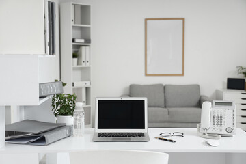 Workplace with laptop, folders and plant in light office