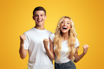 Happy young couple celebrating success with clenched fists, isolated on yellow background. Panorama