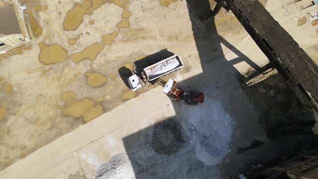 Aerial footage of halite or rock salt being loaded by a wheel front loader on a bulk cargo tipper truck. Drone shot of salt being poured in an industrial truck and weighed at a salt mine. Industrial

