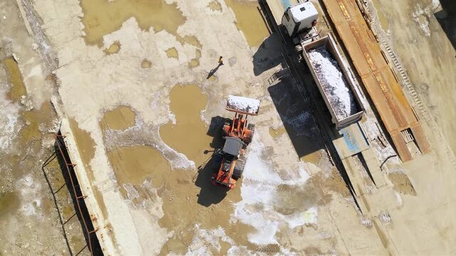 Aerial footage of halite or rock salt being loaded by a wheel front loader on a bulk cargo tipper truck. Drone shot of salt being poured in an industrial truck and weighed at a salt mine. Industrial
