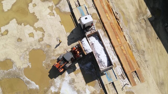 Aerial footage of halite or rock salt being loaded by a wheel front loader on a bulk cargo tipper truck. Drone shot of salt being poured in an industrial truck and weighed at a salt mine. Industrial
