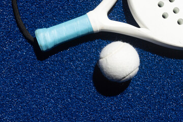 White professional paddle tennis racket and white ball with natural lighting on blue background....