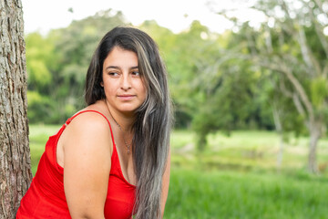 latin woman looking to the side, leaning against a tree with a background of green nature.