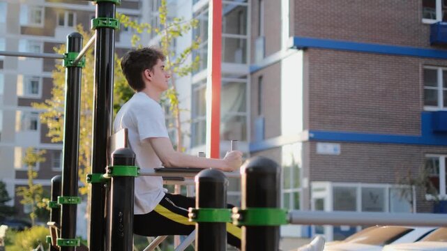 A young thin guy has difficulty doing abdominal exercises on the sports ground